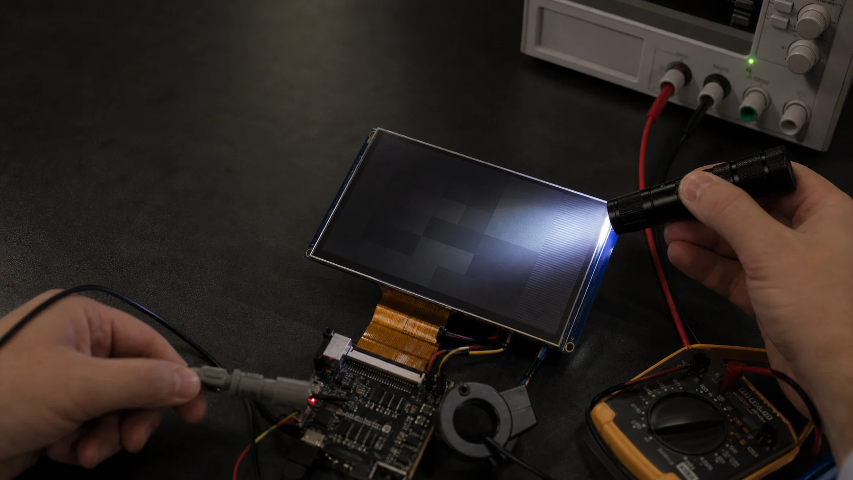 Engineer using a flashlight and multimeter to diagnose an LCD module with an image but no backlight